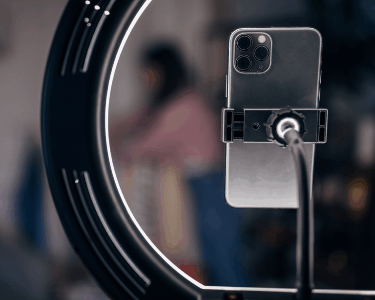 Smartphone preso a suporte com ring light aceso, usado para gravação de conteúdo digital.